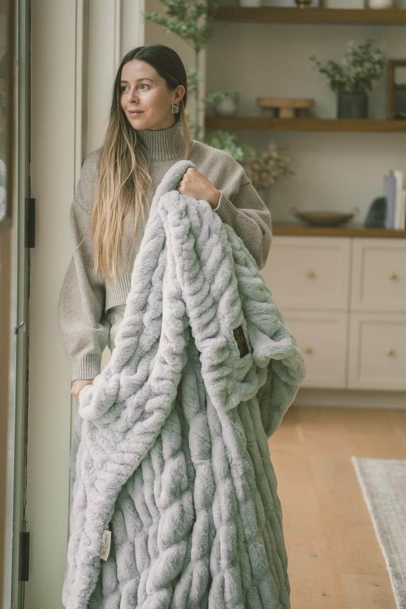 Woman holding a soft Hugs Willow Blue Blanket in a cozy indoor setting.