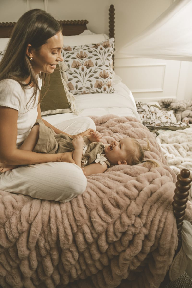 Mom and baby enjoying quality time on a soft Hugs Heirloom Rose Blanket in a cozy bedroom setting.