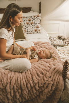 Mom and baby enjoying quality time on a soft Hugs Heirloom Rose Blanket in a cozy bedroom setting.