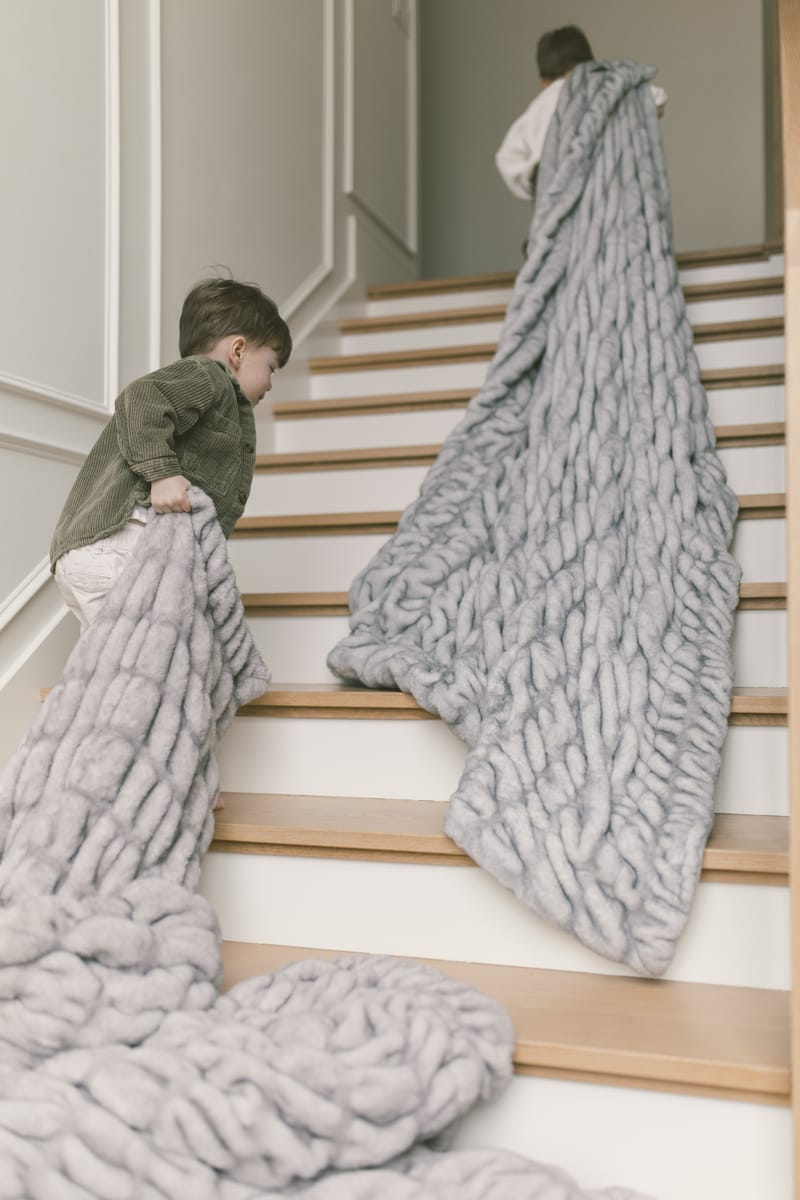 Two children carrying the Hugs Moonbeam Blanket up the stairs, showcasing its cozy and modern design.
