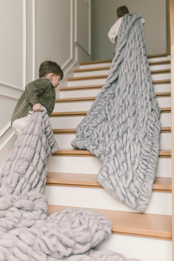 Two children carrying the Hugs Moonbeam Blanket up the stairs, showcasing its cozy and modern design.