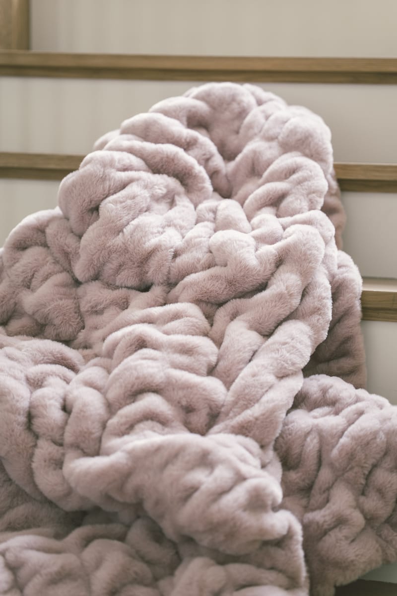 Hugs Heirloom Rose Blanket draped on a wooden surface, showcasing its soft purple-pink hue and plush texture.