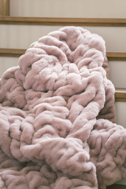Hugs Heirloom Rose Blanket draped on a wooden surface, showcasing its soft purple-pink hue and plush texture.