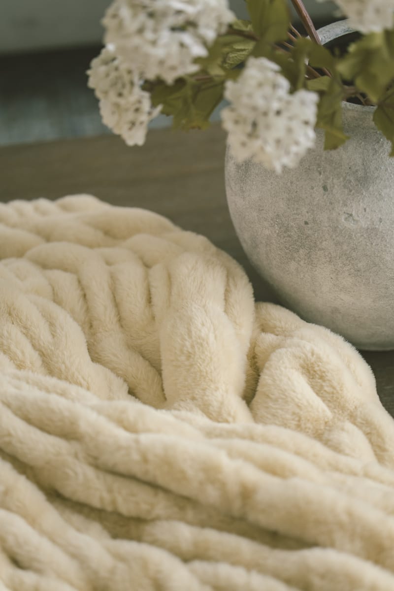 Cozy yellow Hugs Honey Butter Blanket with a vase of white flowers in the background.