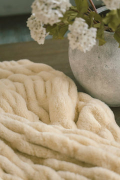 Cozy yellow Hugs Honey Butter Blanket with a vase of white flowers in the background.