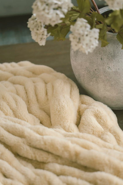 Cozy yellow Hugs Honey Butter Blanket with a vase of white flowers in the background.
