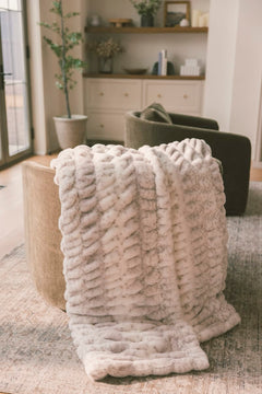 Hugs Cream Fawn Blanket draped over a cozy chair, showcasing its soft texture and fawn-inspired print.