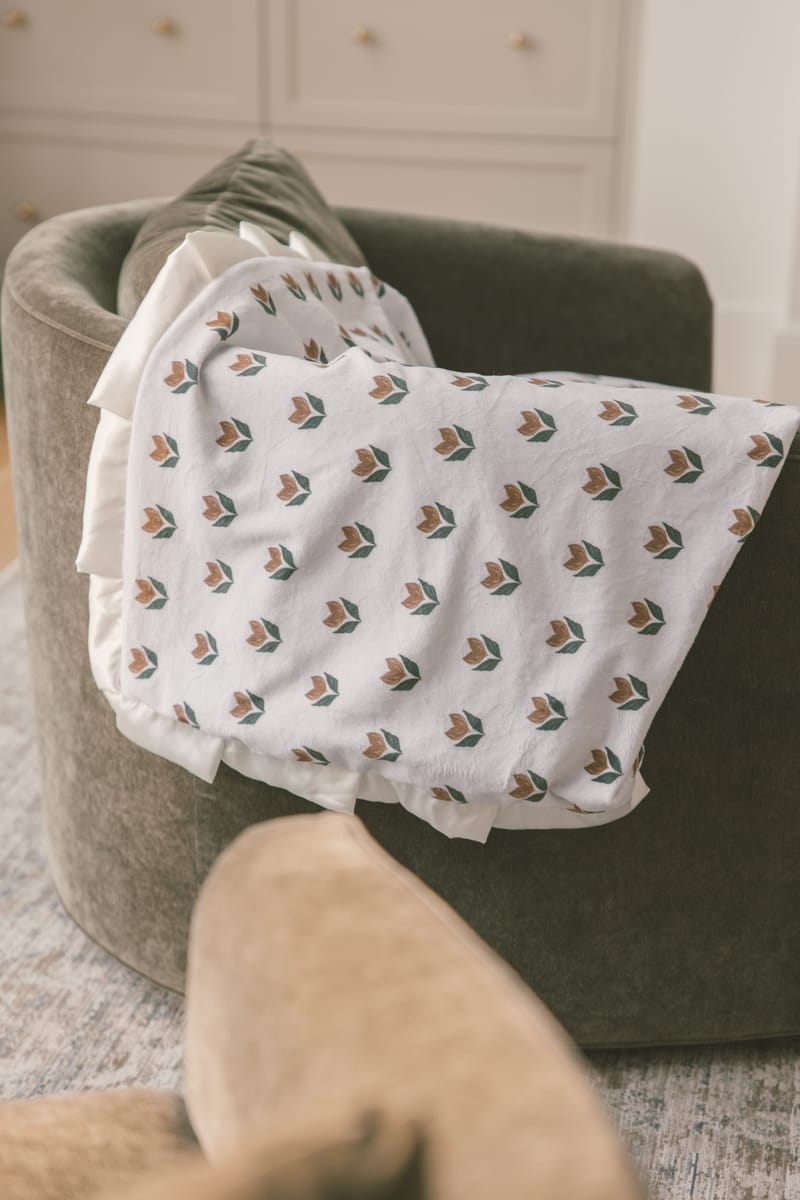 Tulip Garden Blanket draped over a cozy armchair, featuring a delicate tulip pattern on a soft cream background.