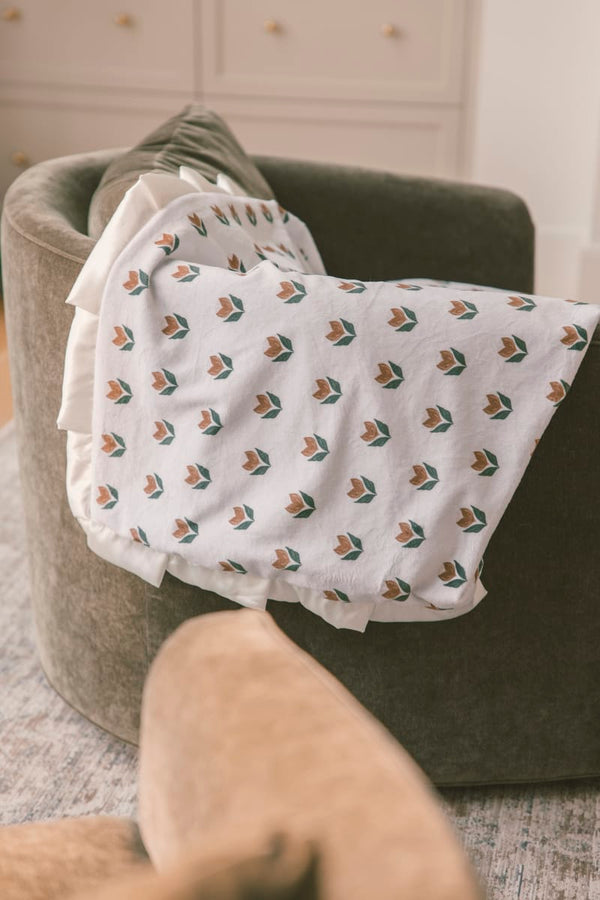 Tulip Garden Blanket draped over a cozy armchair, featuring a delicate tulip pattern on a soft cream background.