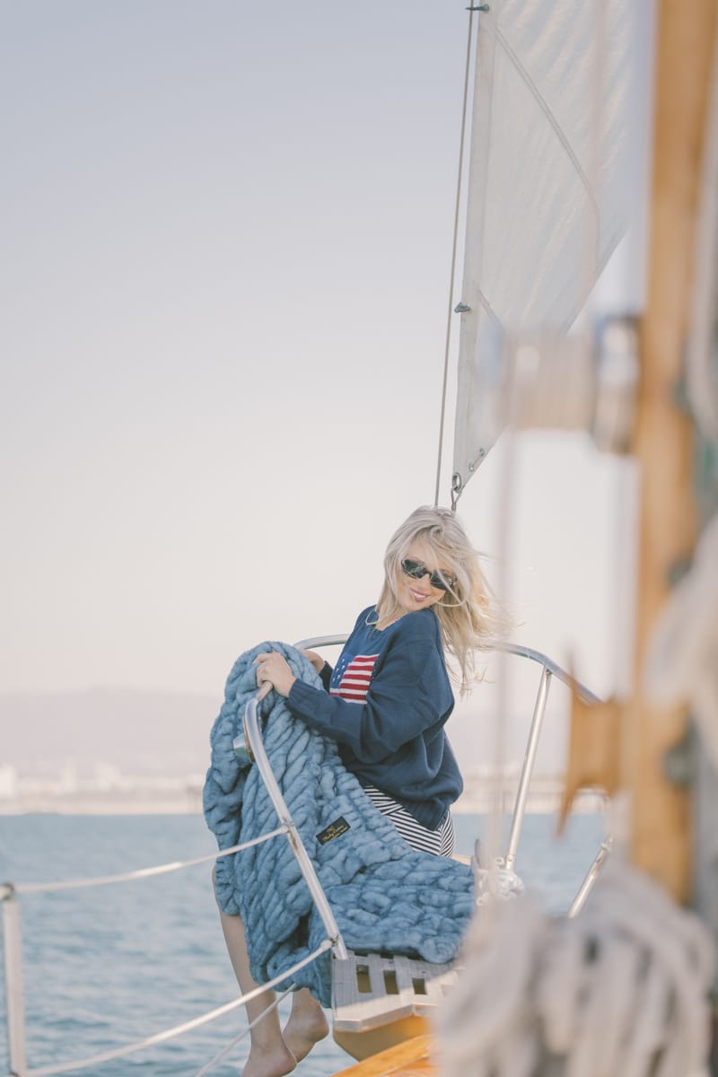 Person on a sailboat holding a blue Minky Couture Hugs blanket with a scenic background