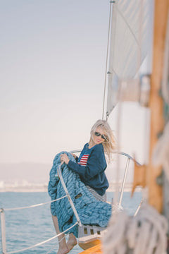 Person on a sailboat holding a blue Minky Couture Hugs blanket with a scenic background
