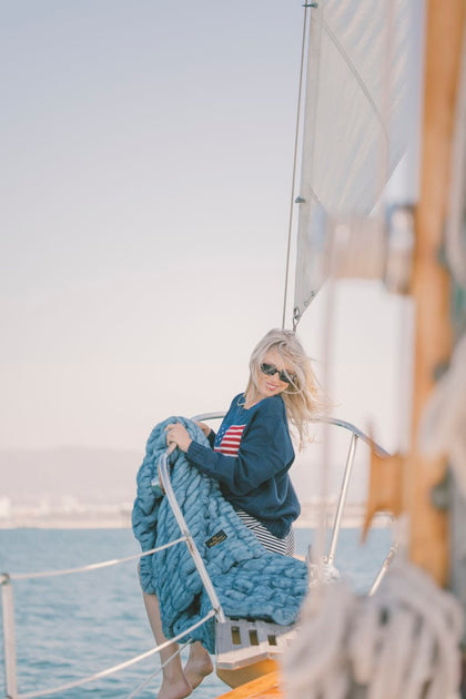 Person on a sailboat holding a blue Minky Couture Hugs blanket with a scenic background