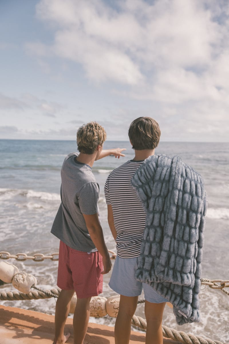 Two people standing by a railing overlooking the ocean with a clear sky with a blue Minky Couture blanket. 