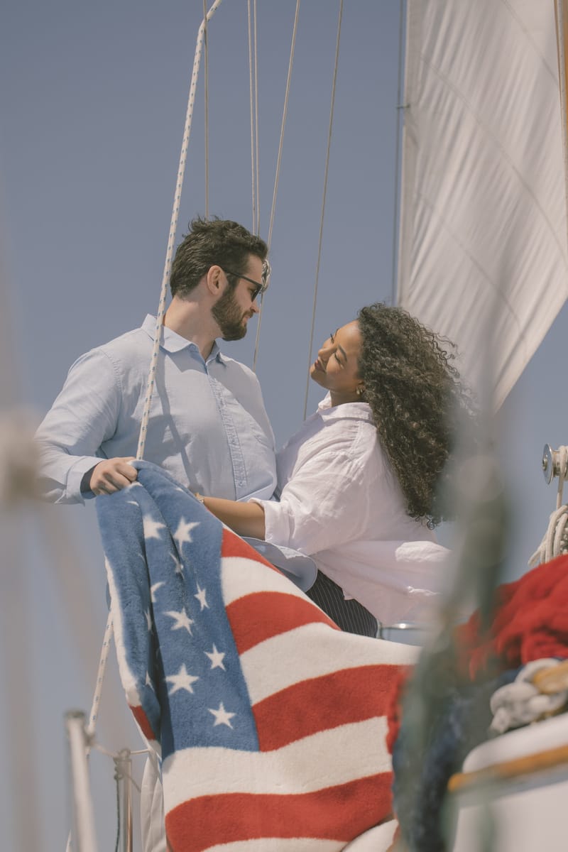 Two people on a sailboat with an American flag blanket