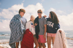 Four people standing on a beach with Minky Couture Hugs blankets and clothing.