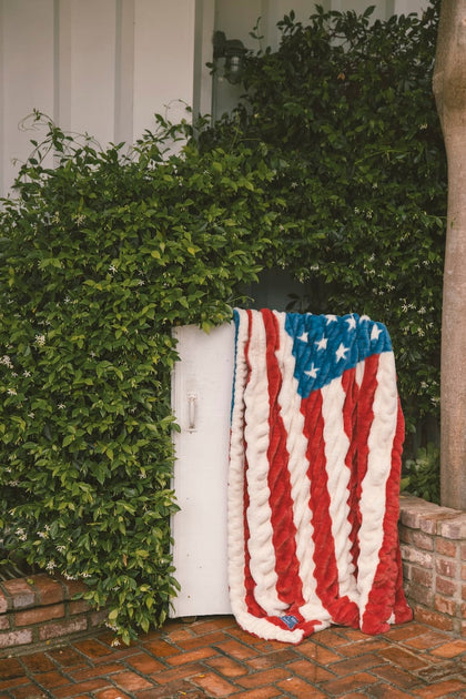 American flag blanket draped over a white door with greenery in the background