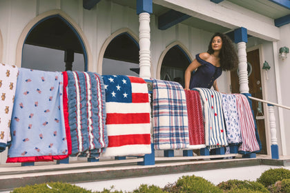 Woman standing on a porch with various patterned blankets, including an American flag design, draped over a railing.