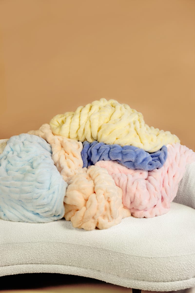 Pastel-colored blankets stacked on a white surface with a beige background