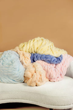 Pastel-colored blankets stacked on a white surface with a beige background