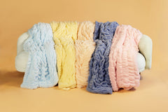Five textured blankets in blue, yellow, orange, purple, and pink on a beige background