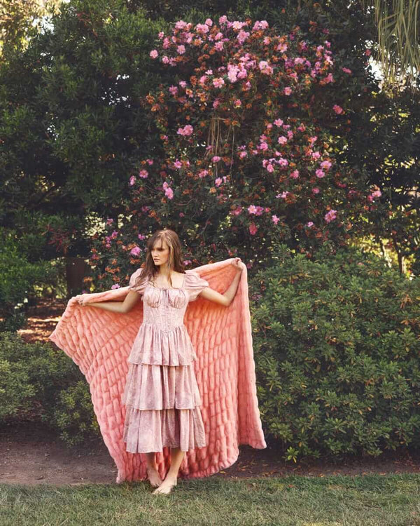 Hugs Peach Blanket draped over a model in a garden with blooming flowers, showcasing its soft texture and color.