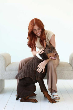 A woman sitting with a Doberman wearing a plush Pet Vest in Cream/Dark Brown, showcasing comfort and style.