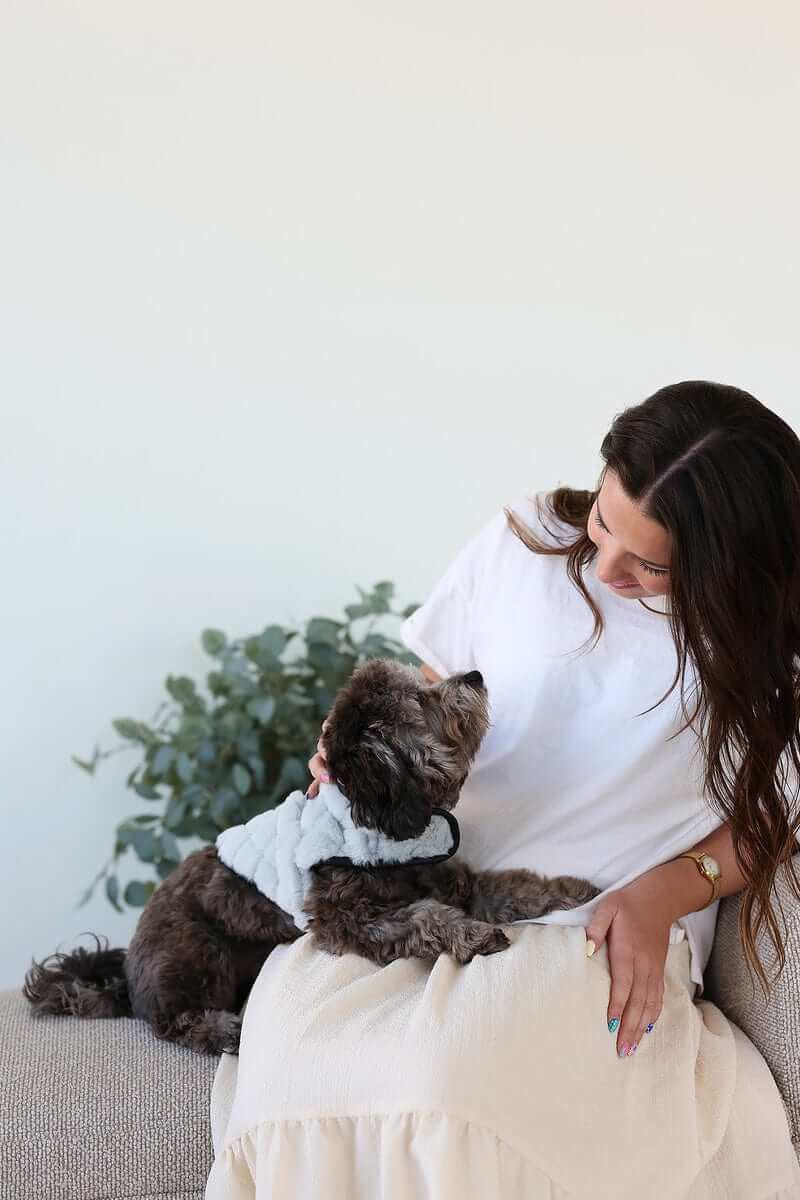 A woman sitting on a couch with a dog wearing a Pet Vest Dark/Light Gray, offering comfort and style.