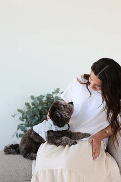 A woman sitting on a couch with a dog wearing a Pet Vest Dark/Light Gray, offering comfort and style.