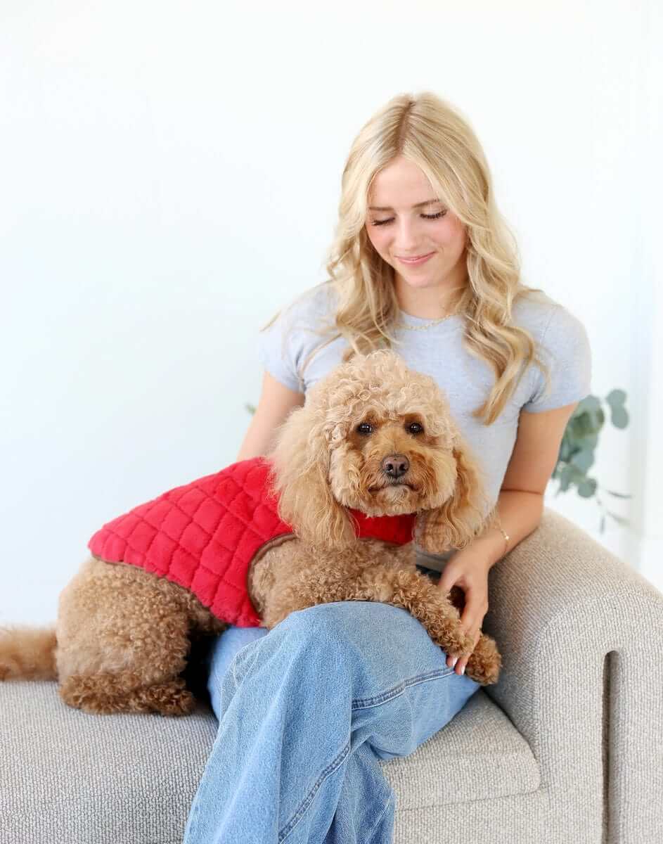 A woman sits on a couch with a dog wearing a Pet Vest in Red/Cream, showcasing its plush comfort and stylish design.