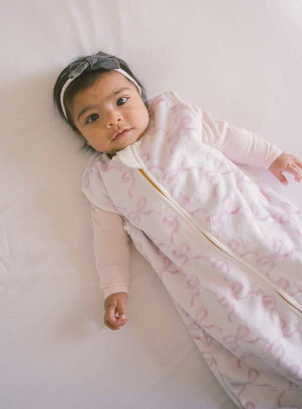 Infant wearing Pretty Pink Bows Wearable Minky Blanket, showcasing safe and cozy sleep alternative.