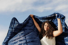 A woman joyfully displaying the Sorbet Navy Blanket against a blue sky.