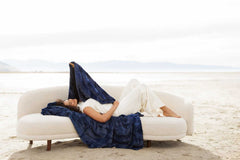 Woman relaxing on a couch draped with Sorbet Navy Blanket, showcasing its plush, textured finish and rich blue hue.