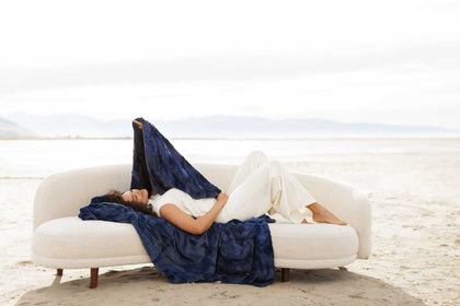 Woman relaxing on a couch draped with Sorbet Navy Blanket, showcasing its plush, textured finish and rich blue hue.
