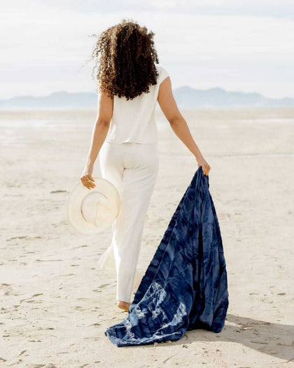 Woman walking on beach with Sorbet Navy Blanket in hand, showcasing its soft texture and rich navy blue color.
