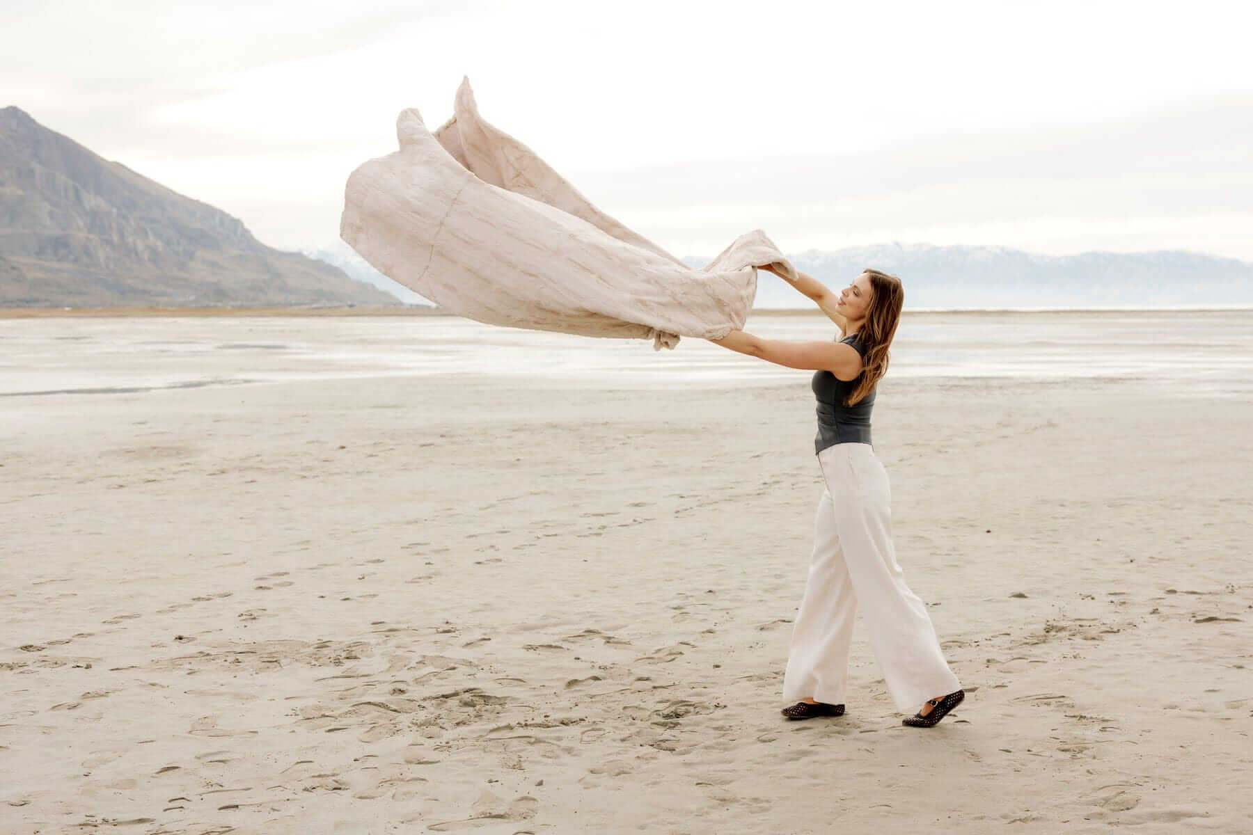 Woman joyfully waving the Sorbet Almond Croissant Blanket in a serene beach setting.
