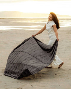 Model showcasing the Sorbet Charcoal Blanket on the beach during sunset, highlighting its plush texture and deep gray color.