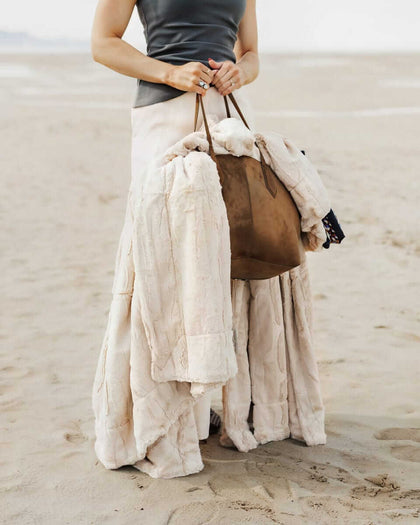 Woman holding a Sorbet Almond Croissant Blanket and a brown bag on the beach.