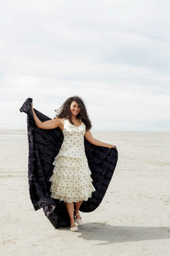 Woman wearing a polka dot dress on the beach, showcasing the Sorbet Black Blanket.