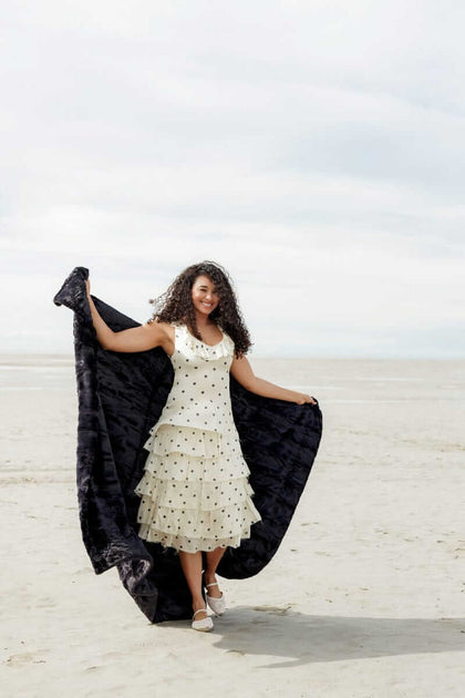 Woman wearing a polka dot dress on the beach, showcasing the Sorbet Black Blanket.