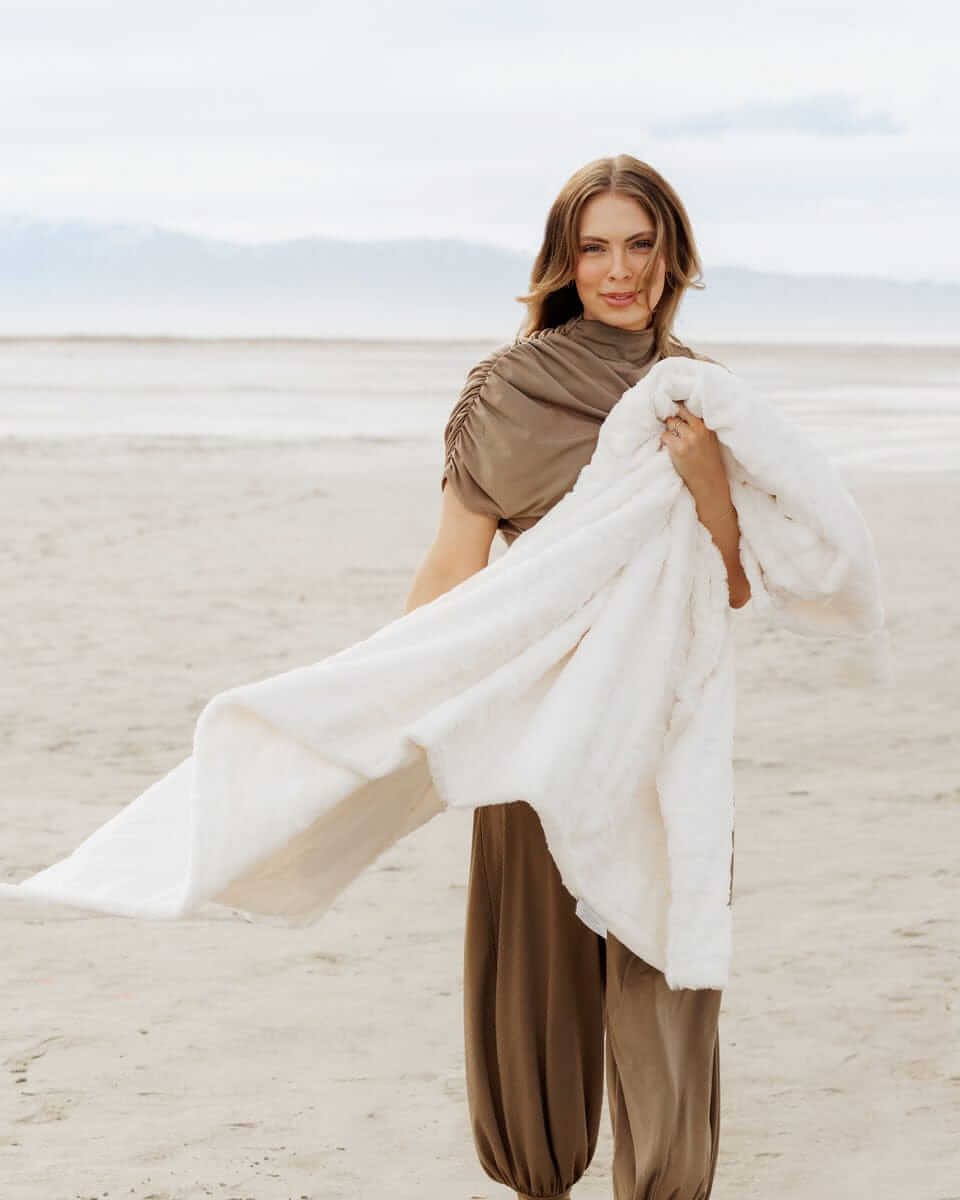 Woman on the beach holding a Sorbet Vanilla Blanket, showcasing its silky smooth texture and elegance.