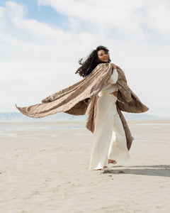 Woman joyfully wearing the Sorbet Milk Chocolate Blanket on a beach, showcasing its rich texture and warm color.