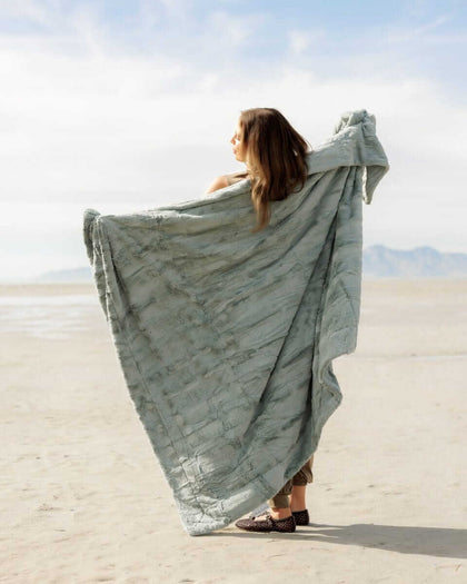 Woman draped in a Sorbet Mist Blanket, showcasing its gentle green hue and textured feel at the beach.