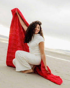 Woman on the beach showcasing the Sorbet Red Blanket, radiating vibrant color and comfort.