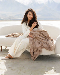 A woman sitting on a couch holding a Sorbet Milk Chocolate Blanket, exuding comfort and warmth.
