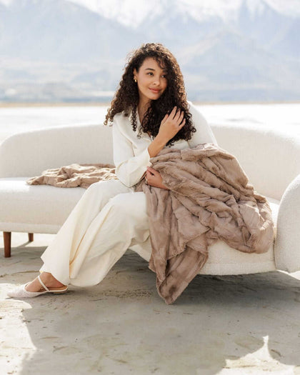 A woman sitting on a couch holding a Sorbet Milk Chocolate Blanket, exuding comfort and warmth.