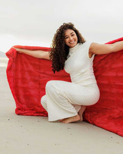 Sorbet Red Blanket showcased by a woman on the beach, emphasizing its vibrant color and luxurious texture.