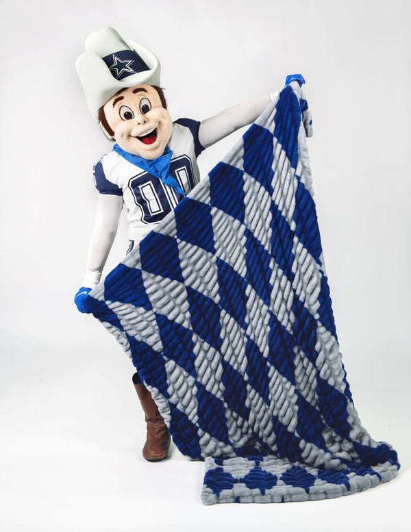 A Dallas Cowboys mascot in a white cowboy hat and football uniform holds up a large plush throw blanket with a blue and gray argyle pattern against a white studio background.