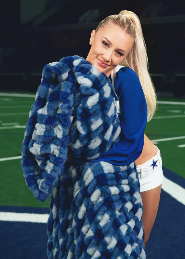 A Dallas Cowboys cheerleader standing on a football field whole holding a blue and charcoal gingham patterned blanket.