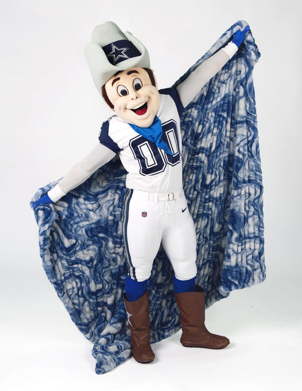 A Dallas Cowboys mascot in a white and blue football uniform stands against a light gray studio background, holding up a blue and white marbled blanket. 