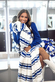 A woman wearing a plush faux fur blanket with blue and white stripes, styled with a matching blue sweatshirt and white cowboy boots in a modern indoor setting.